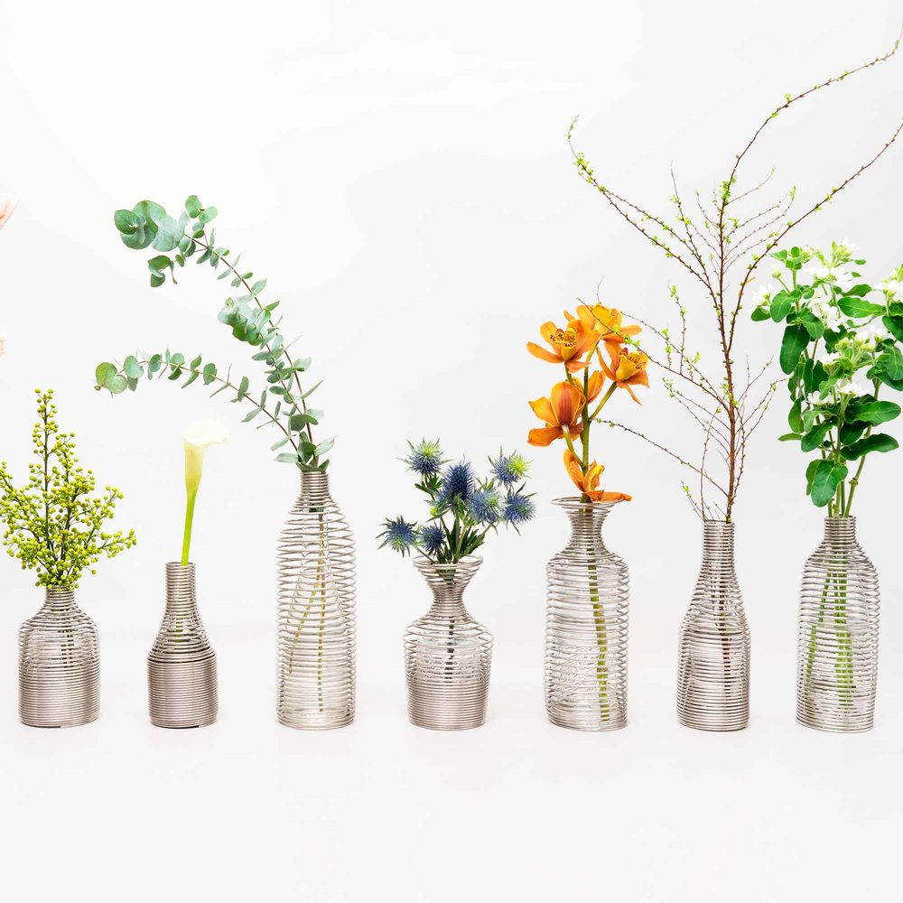 線を密に巻いてつくった花器。花や枝を生けたものが並んでいる
